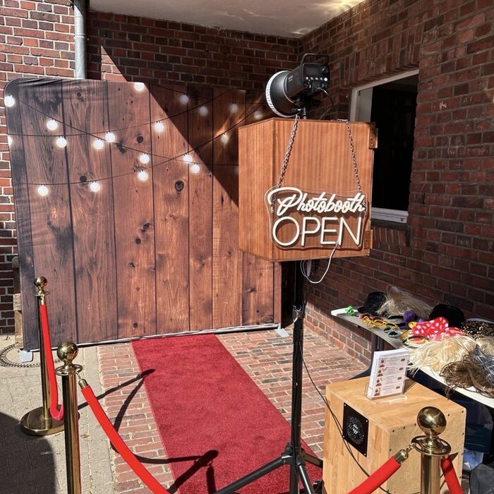 Fotobox mit leuchtendem 'Photobooth Open'-Schild und rotem Teppich